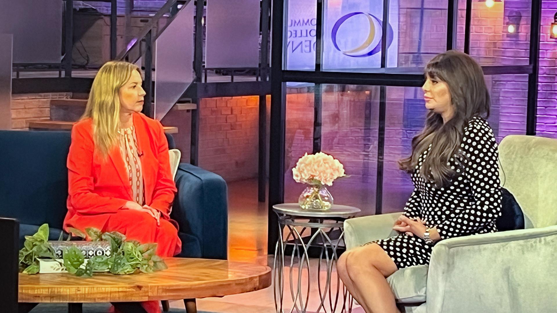 Dr. DeSanctis in red business attire sitting down talking to a woman with long, brown hair. 